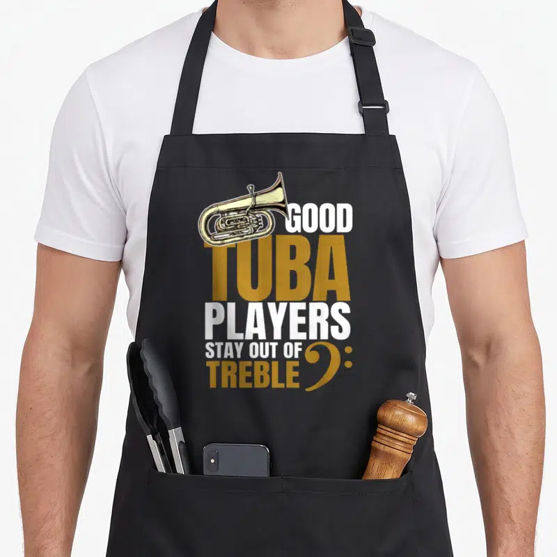 Player tuba apron - Gold tuba illustration with Good Tuba Players Stay Out of Treble text and bass clef symbol — shown on a black cotton canvas apron against a white background