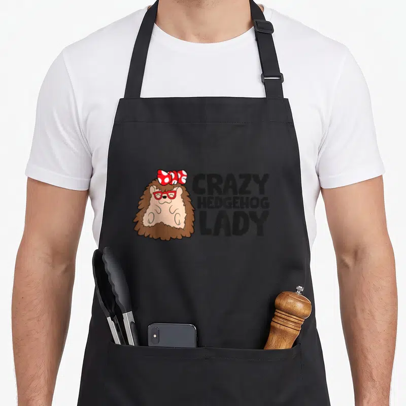 Vintage crazy hedgehog lady apron - Cartoon hedgehog with red glasses and spotted bow next to stacked text — shown on a black cotton canvas apron against a white background