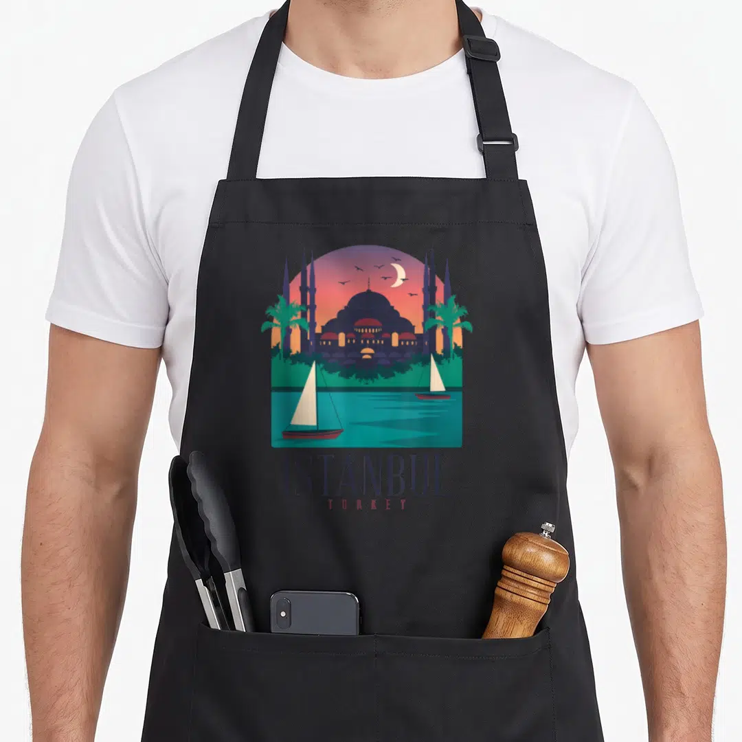 Istanbul turkey apron - Minimalist mosque and sailboat illustration with ISTANBUL TURKEY text in blue and orange — shown on a black cotton canvas apron against a white background