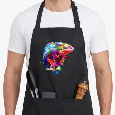 Panther chameleon apron - Multicolored watercolor chameleon perched on plant with blue red yellow green purple paint — shown on a black cotton canvas apron against a white background