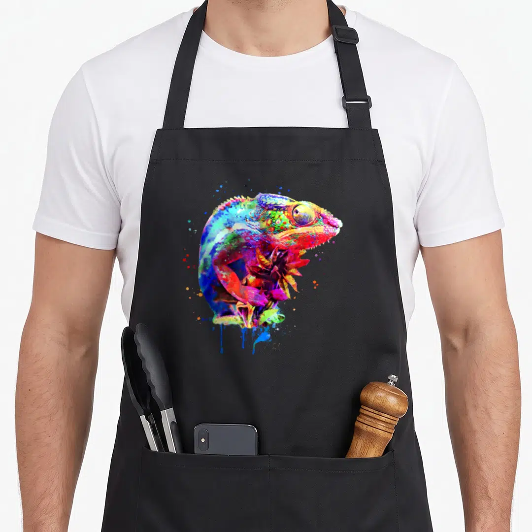 Panther chameleon apron - Multicolored watercolor chameleon perched on plant with blue red yellow green purple paint — shown on a black cotton canvas apron against a white background