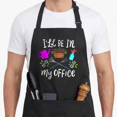 Office gardener apron - I'll Be In My Office text with watering can, flower pot, spray bottle, and crossed rake — shown on a black cotton canvas apron against a white background