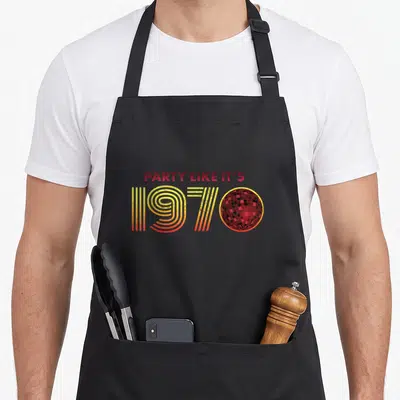Ball halloween apron - Red and yellow 1970 text with disco ball replacing the zero on black background — shown on a black cotton canvas apron against a white background