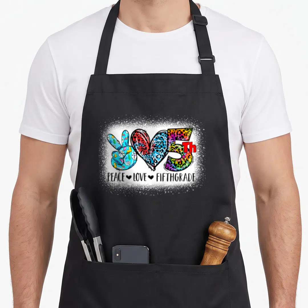 Grade fifth apron - Cartoon peace sign heart and number 5 in multicolored leopard print with PEACE LOVE FIFTHGRADE text — shown on a black cotton canvas apron against a white background