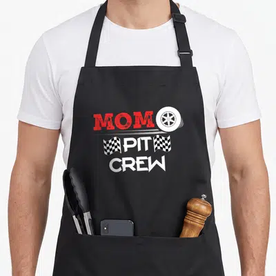 Car racing crew aprons - MOM PIT CREW text with white tire and two checkered flags in red black and white — shown on a black cotton canvas apron against a white background