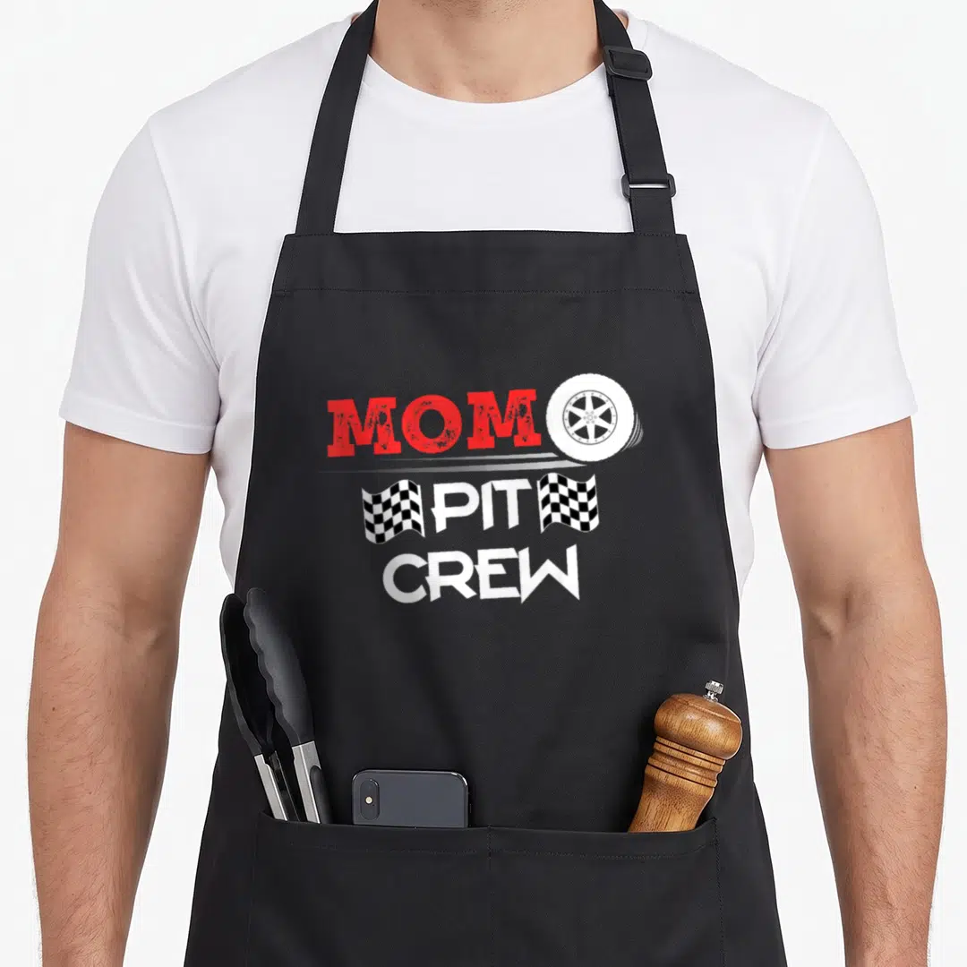 Car racing crew aprons - MOM PIT CREW text with white tire and two checkered flags in red black and white — shown on a black cotton canvas apron against a white background