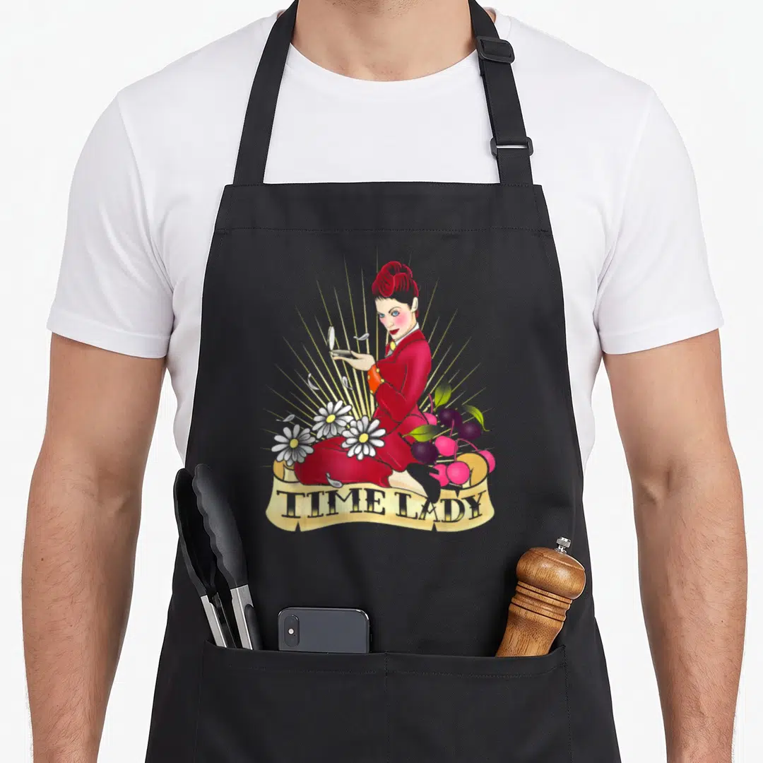 Missy rockabilly apron - Woman in red dress holding compact mirror surrounded by daisies plums and gold rays with TIME — shown on a black cotton canvas apron against a white background