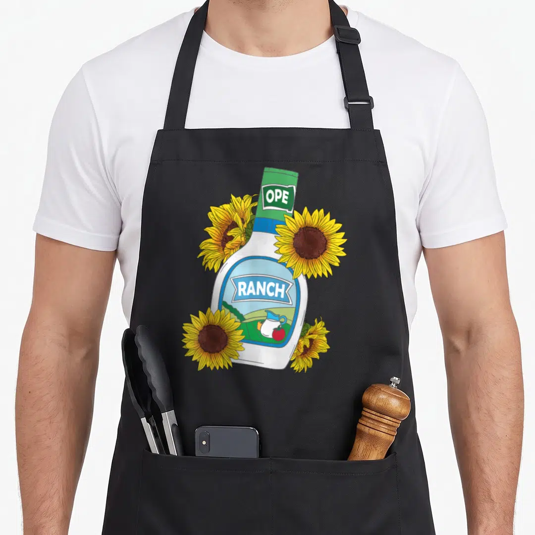 Foodie dressing apron - Cartoon ranch bottle with OPE RANCH text and four yellow sunflowers — shown on a black cotton canvas apron against a white background