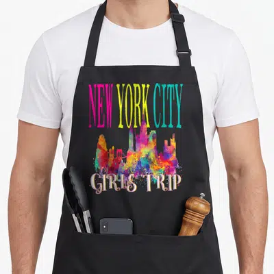 Trip new york apron - Multicolored watercolor New York skyline with pink and yellow text reading girls trip — shown on a black cotton canvas apron against a white background