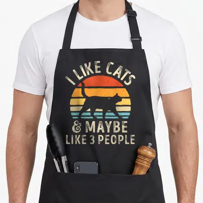 Maybe cat apron - Retro sunset with grey cat silhouette and text I like cats and maybe like 3 people — shown on a black cotton canvas apron against a white background