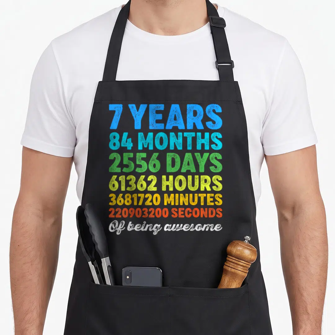 Countdown birthday apron - Stacked colorful text listing 7 years, 84 months, and seconds of being awesome — shown on a black cotton canvas apron against a white background