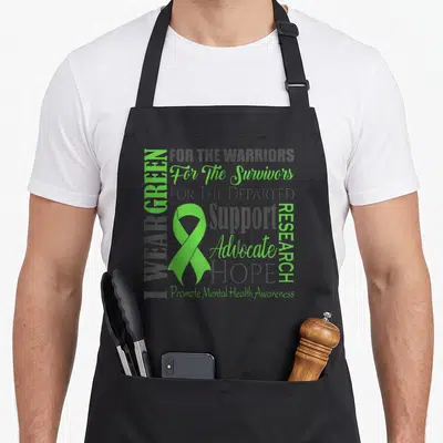 Funny matter mental health awareness apron - Green ribbon and vertical text I WEAR GREEN with support phrases on grey — shown on a black cotton canvas apron against a white background