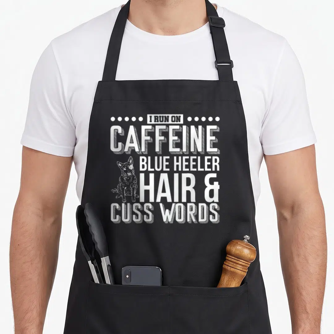Run hair apron - White stacked text reading I Run On Caffeine Blue Heeler Hair and Cuss Words with a small dog sitting — shown on a black cotton canvas apron against a white background