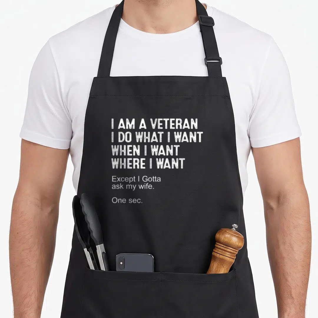 Sarcasm father day apron - White stacked typography reading I am a veteran except I gotta ask my wife on black fabric — shown on a black cotton canvas apron against a white background