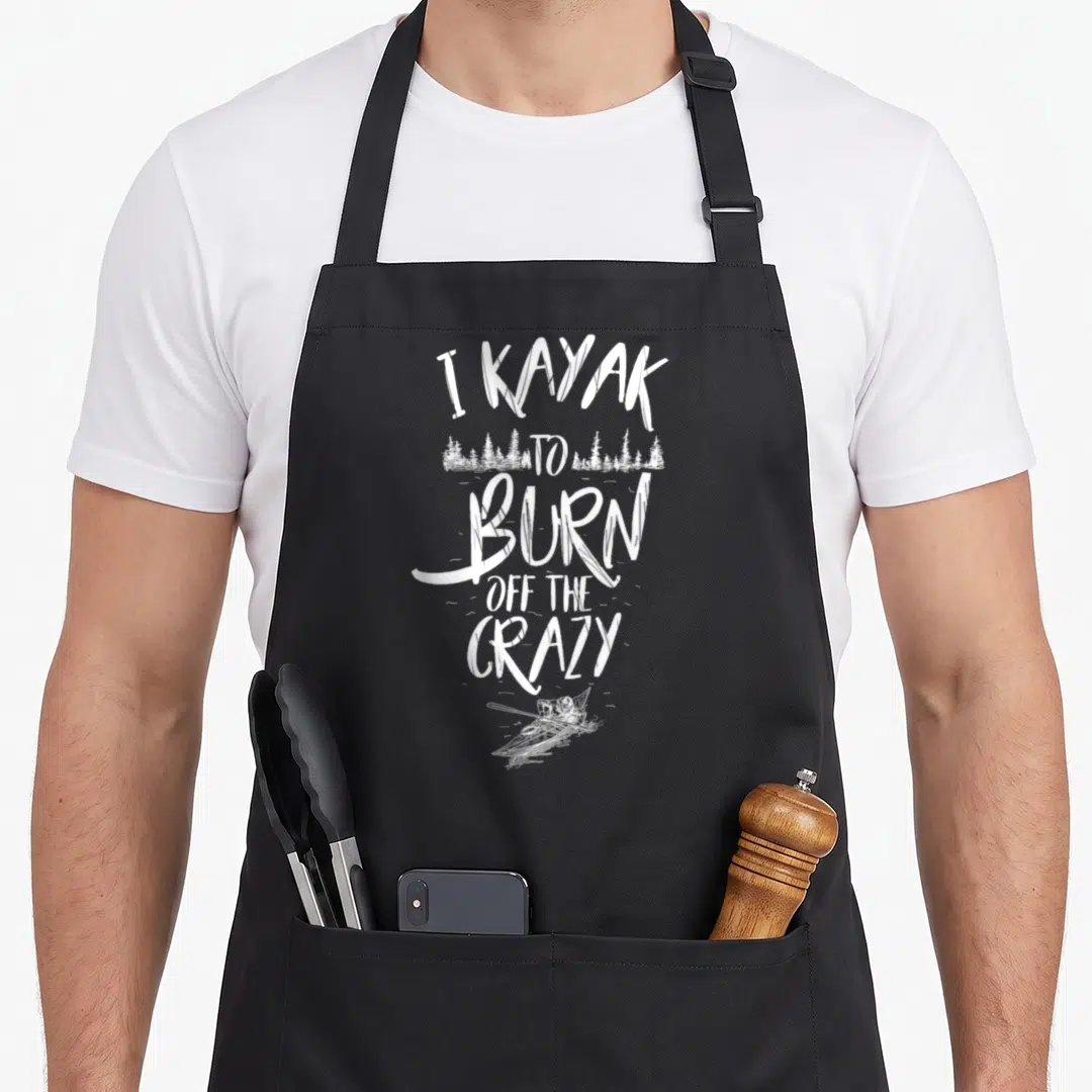 Kayaker kayak girl apron - White distressed text I KAYAK TO BURN OFF THE CRAZY with forest and kayaker silhouette — shown on a black cotton canvas apron against a white background