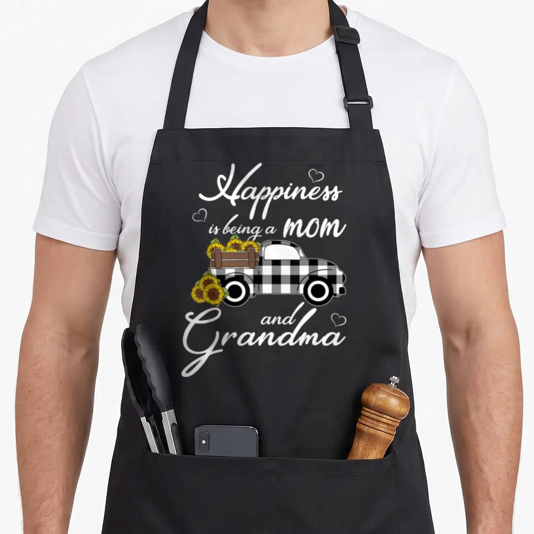 Happiness truck apron - Buffalo plaid truck carrying sunflowers with white script text and hearts — shown on a black cotton canvas apron against a white background