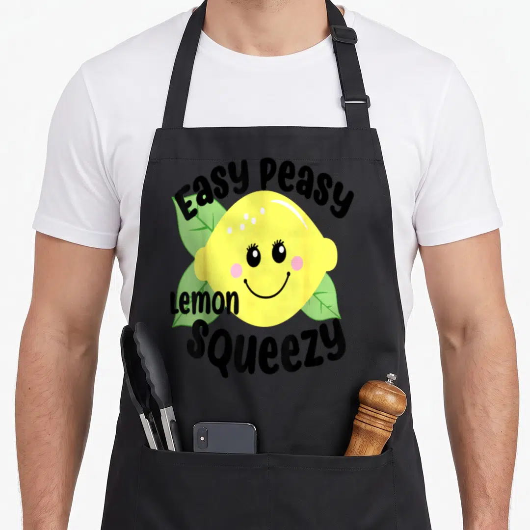 Easy lemon apron - Smiling yellow cartoon lemon with green leaves and Easy Peasy Lemon Squeezy text in black — shown on a black cotton canvas apron against a white background