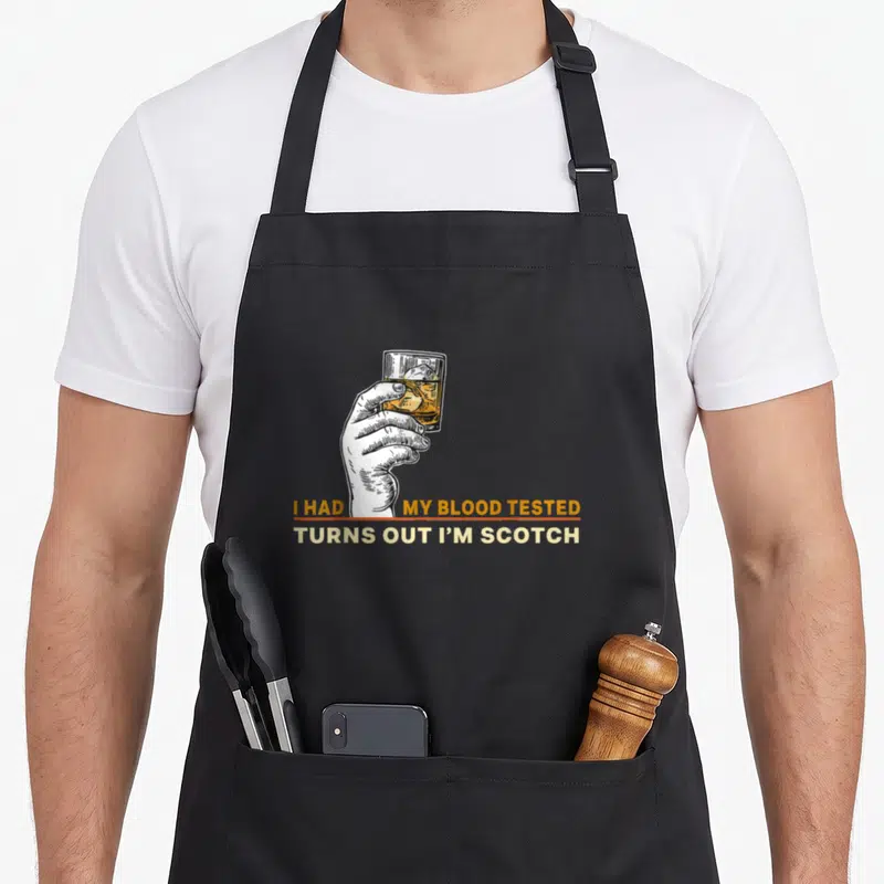 Tested blood apron - Hand holding scotch glass with I Had My Blood Tested Turns Out I'm Scotch text — shown on a black cotton canvas apron against a white background