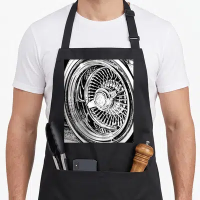 Spoke car apron - Black and white photo of a chrome multi-spoke wire car wheel and tire — shown on a black cotton canvas apron against a white background