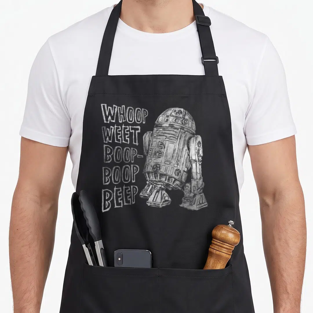 Droid outline of an apron - Distressed white sketch of R2-D2 next to stacked words WHOOP WEET BOOP BOOP BEEP on grey — shown on a black cotton canvas apron against a white background