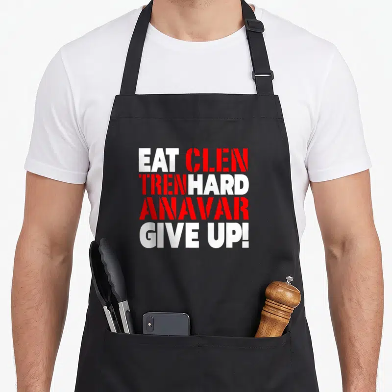 Eat hard quotes apron - Stacked white and red text reading EAT CLEN TREN HARD ANAVAR GIVE UP on black background — shown on a black cotton canvas apron against a white background