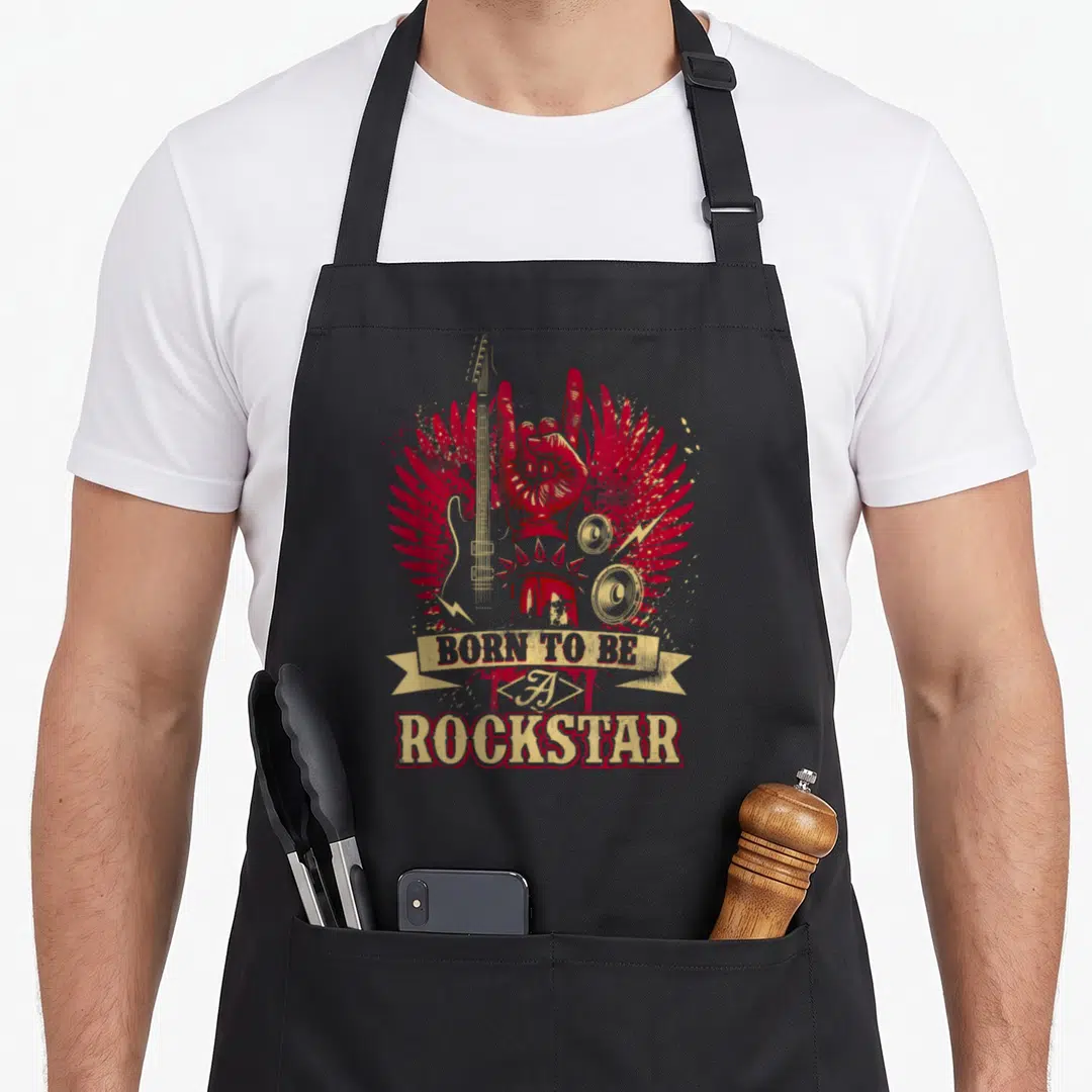 Rock band lover apron - Red winged hand holding horns flanked by gold guitar and speakers with BORN TO BE A ROCKSTAR — shown on a black cotton canvas apron against a white background