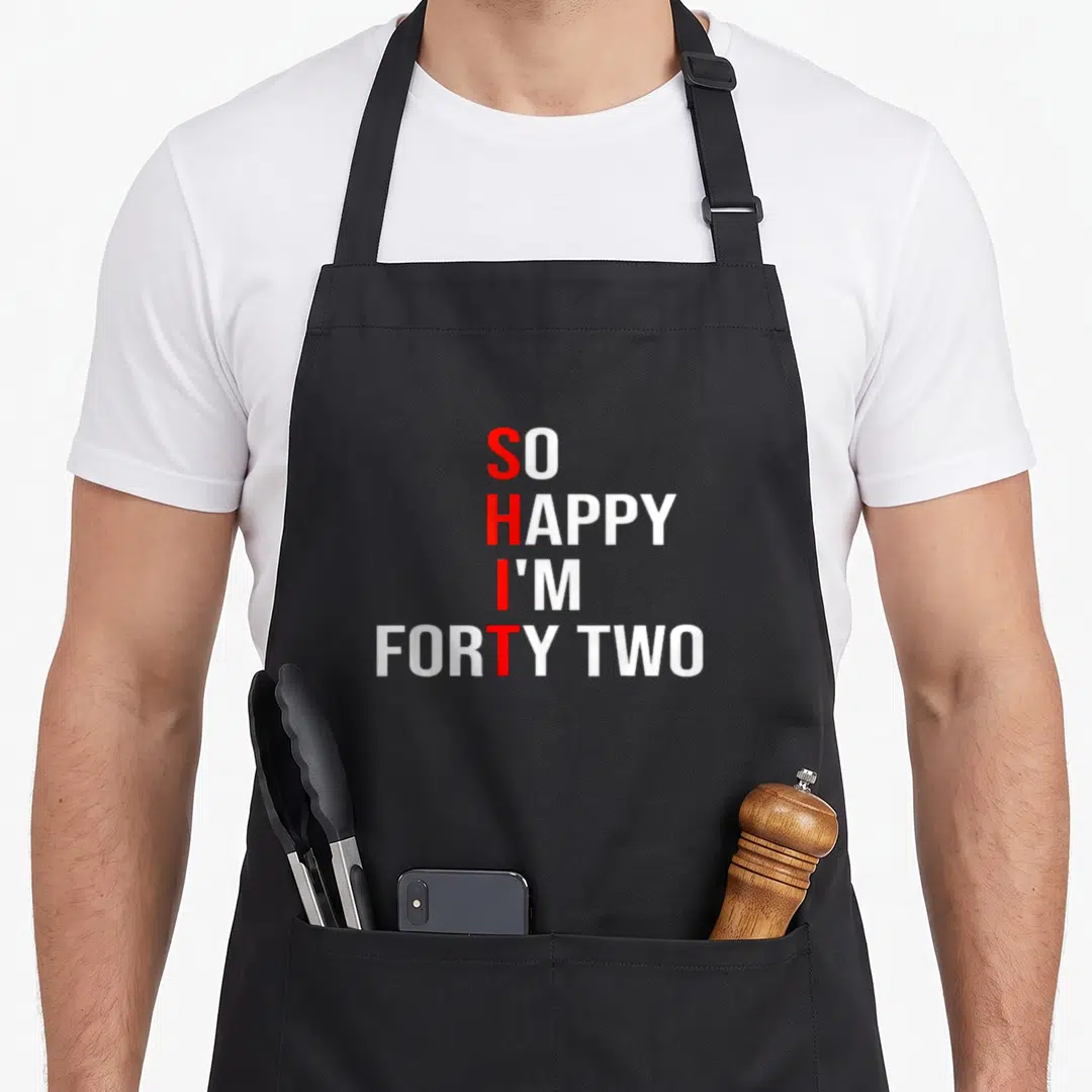 Forty 42nd birthday apron - Red and white stacked text reading So Happy I'm Forty Two with vertical SHIT acronym — shown on a black cotton canvas apron against a white background