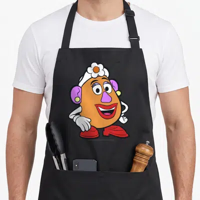 Potato portrait mrs apron - Cartoon potato character with purple nose, red shoes, and white flower hat — shown on a black cotton canvas apron against a white background