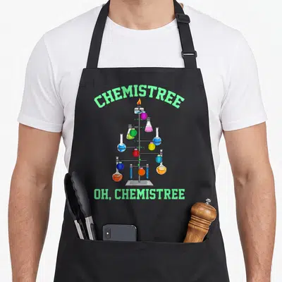 Tree chemistry apron - Cartoon flask Christmas tree with arched CHEMISTREE text and colored liquids — shown on a black cotton canvas apron against a white background