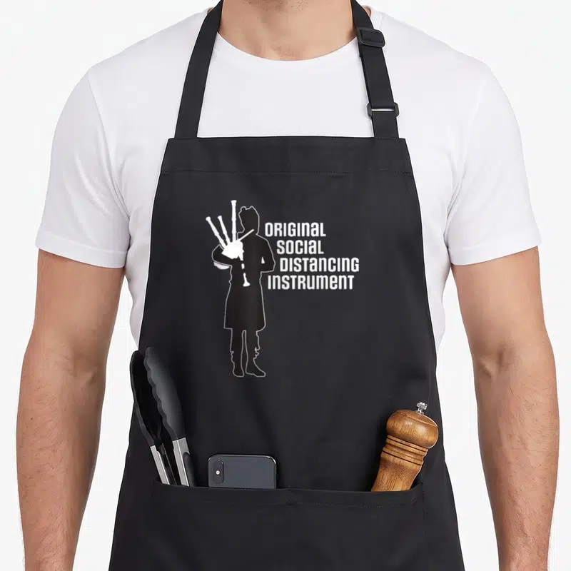 Social bagpipes apron - Black piper silhouette beside stacked white text original social distancing instrument — shown on a black cotton canvas apron against a white background