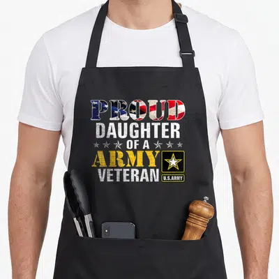 Daughter american flag apron - Stacked text PROUD DAUGHTER OF A ARMY VETERAN with flag fill pattern and black star badge — shown on a black cotton canvas apron against a white background