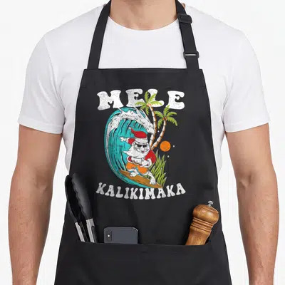 Mele kalikimaka christmas santa apron - Surfing Santa in red hat and orange shorts riding a blue wave under white — shown on a black cotton canvas apron against a white background