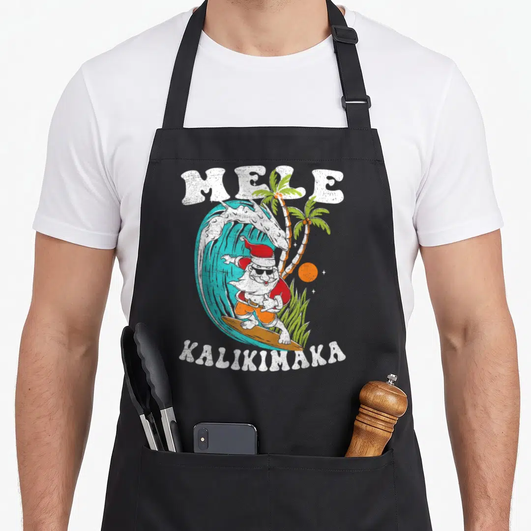 Mele kalikimaka christmas santa apron - Surfing Santa in red hat and orange shorts riding a blue wave under white — shown on a black cotton canvas apron against a white background