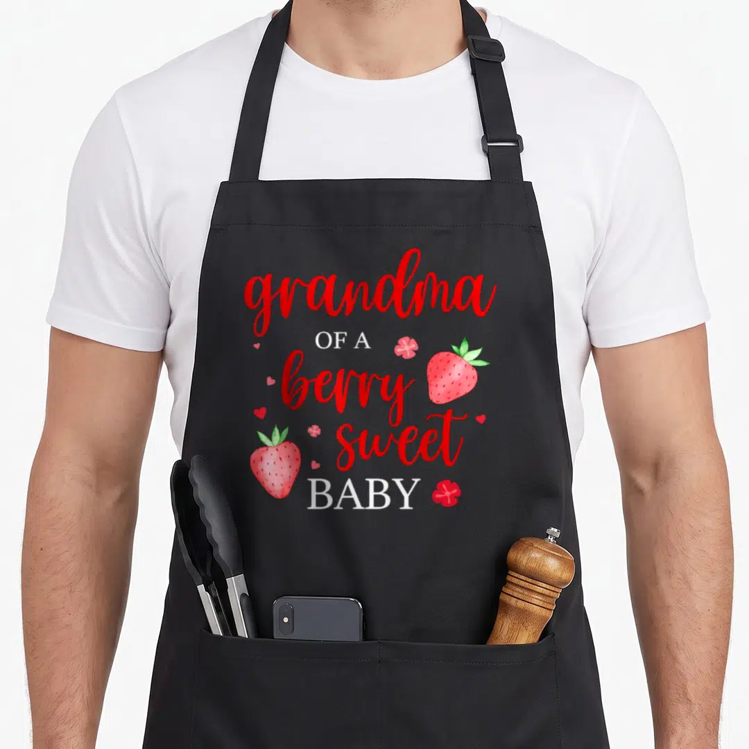 Berry grandma apron - Grandma of a berry sweet baby strawberry pun text with watercolor fruit art — shown on a black cotton canvas apron against a white background