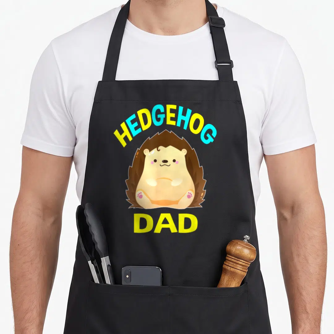 Hedgehog daddy apron - Cartoon hedgehog sitting between yellow HEDGEHOG and DAD text — shown on a black cotton canvas apron against a white background