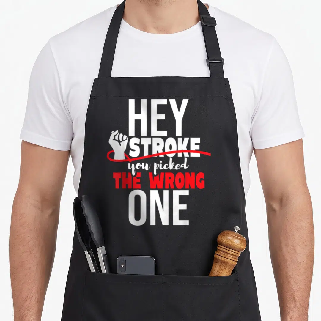 Hey ribbon apron - White clenched fist next to HEY STROKE text with red curved line underlining — shown on a black cotton canvas apron against a white background