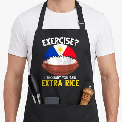 Rice an extra apron - Cartoon bowl of white rice in front of Philippine flag with exercise pun text — shown on a black cotton canvas apron against a white background
