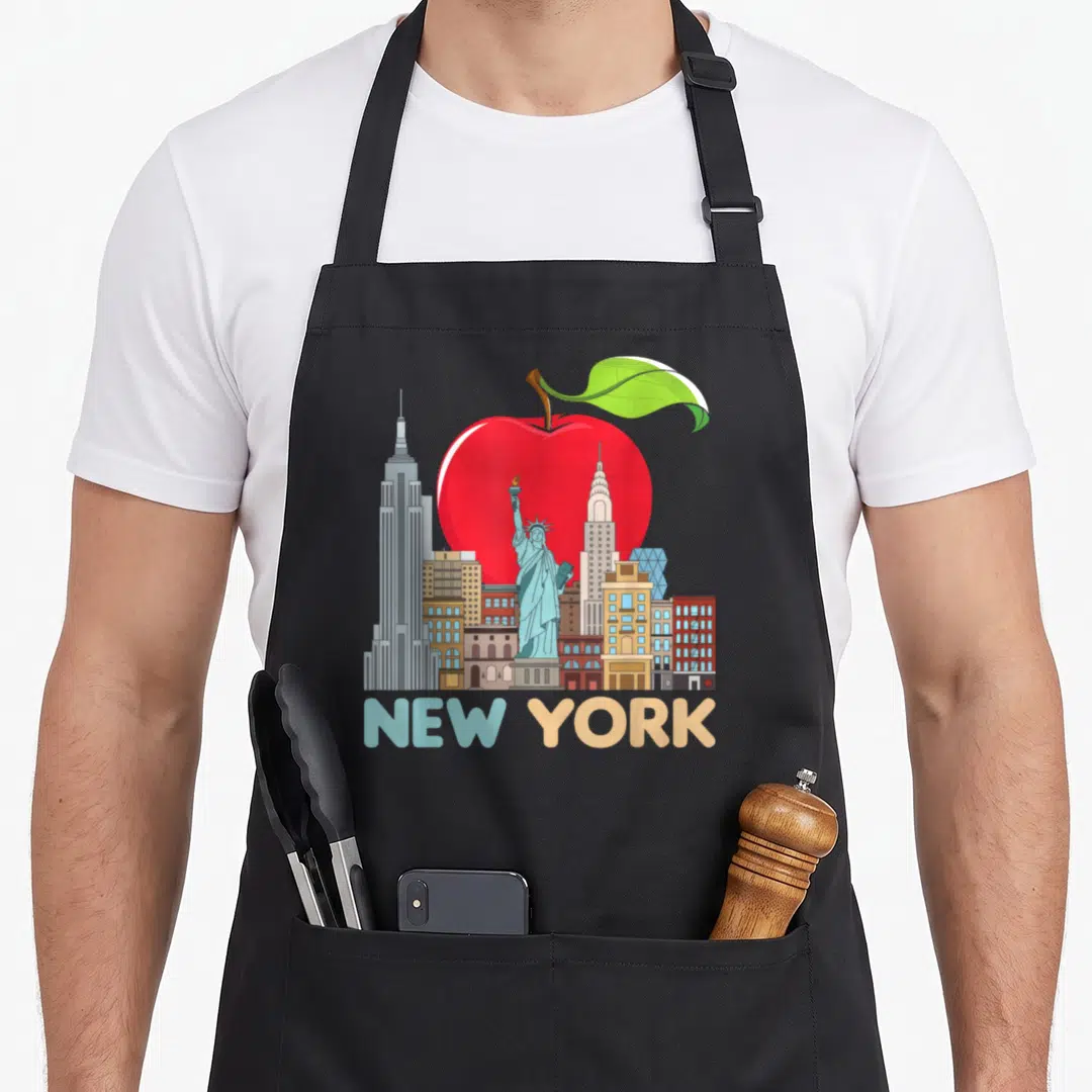 Skyline new york apron - Red apple behind Statue of Liberty and skyscrapers with NEW YORK text in blue and beige — shown on a black cotton canvas apron against a white background