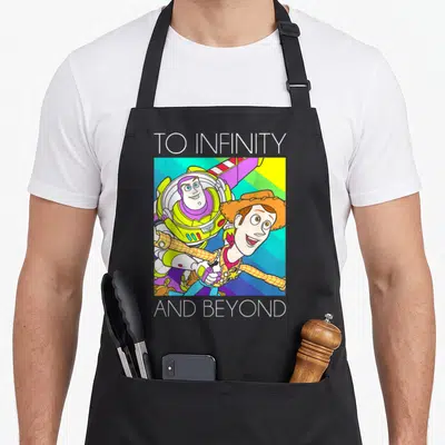 Buzz infinity apron - Buzz Lightyear and Woody cartoon graphic with TO INFINITY AND BEYOND text — shown on a black cotton canvas apron against a white background