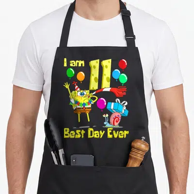 Retro age birthday apron for grilling - SpongeBob holding a party blower with balloons and text I am 11 Best Day Ever — shown on a black cotton canvas apron against a white background