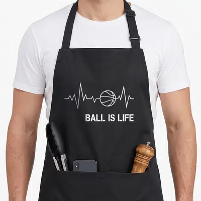 Basketball jump player apron - White heartbeat line with basketball center and BALL IS LIFE text below — shown on a black cotton canvas apron against a white background