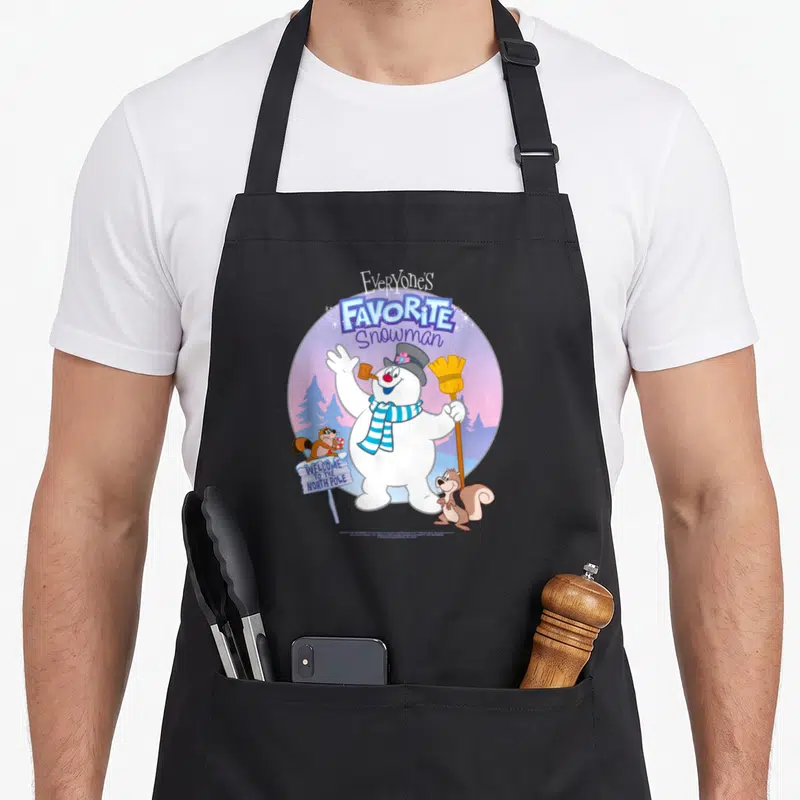 Themed snowman apron - Cartoon snowman waving with broom under Everyone's Favorite Snowman text flanked by two squirrels — shown on a black cotton canvas apron against a white background