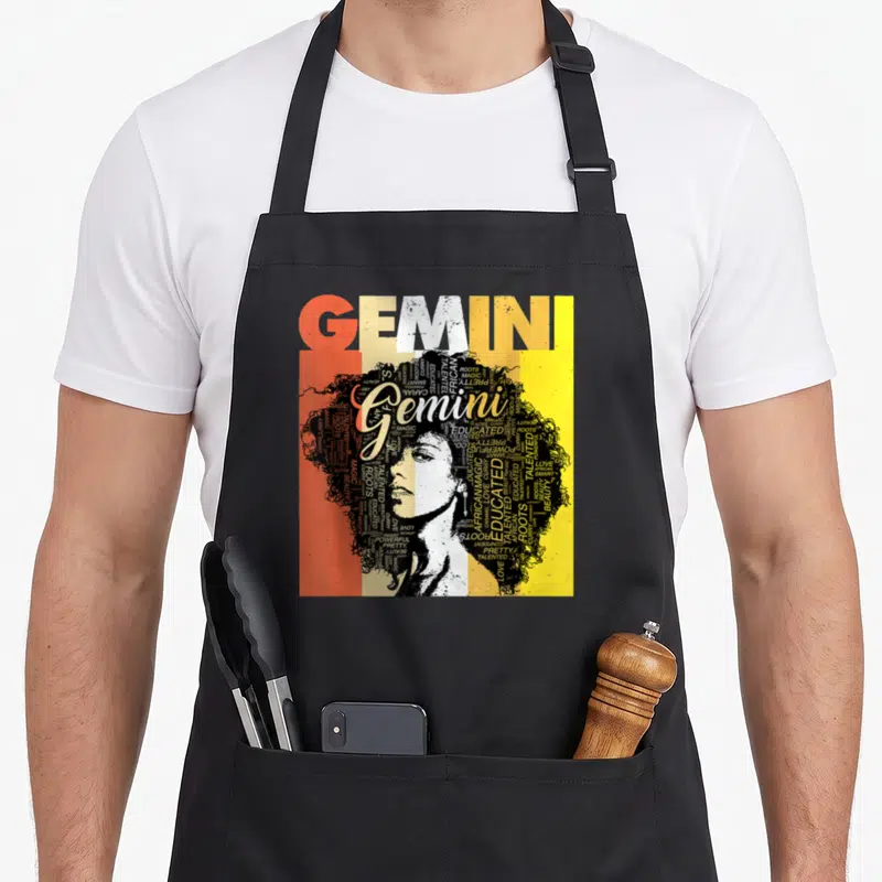Gemini pride hair apron - Typographic woman portrait with afro made of words GEMINI ROOTS MAGIC CURRY in orange beige — shown on a black cotton canvas apron against a white background