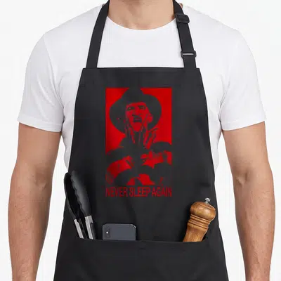 Nightmare prey love apron - White man silhouette with hat and knife on red background with NEVER SLEEP AGAIN text — shown on a black cotton canvas apron against a white background