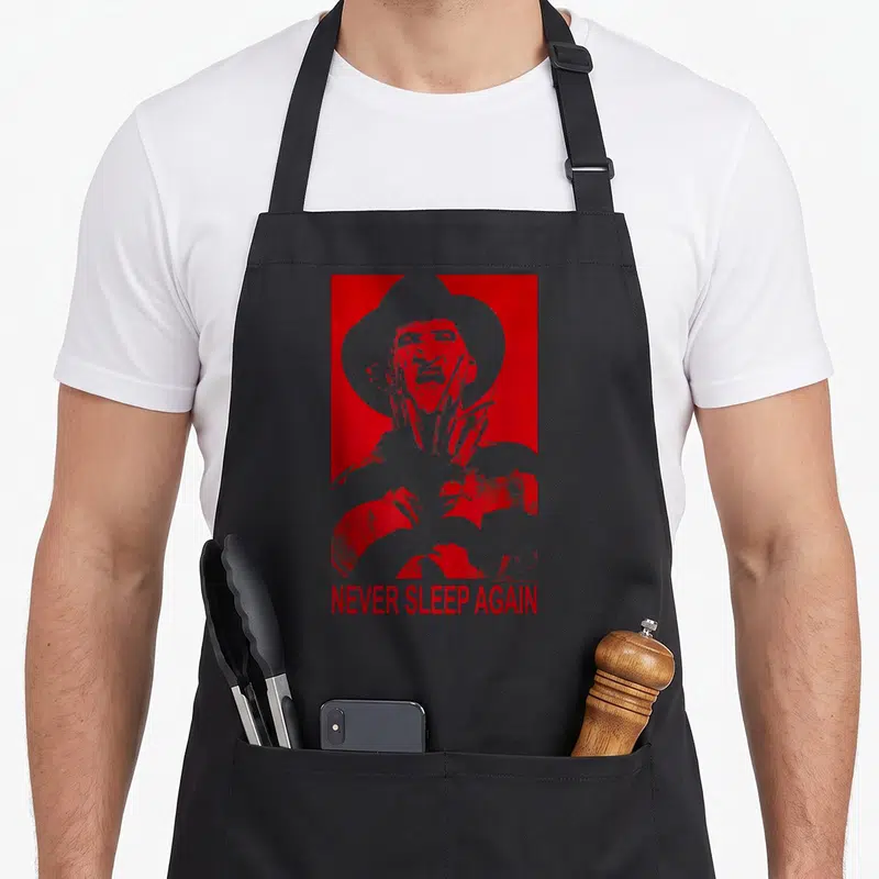 Nightmare prey love apron - White man silhouette with hat and knife on red background with NEVER SLEEP AGAIN text — shown on a black cotton canvas apron against a white background