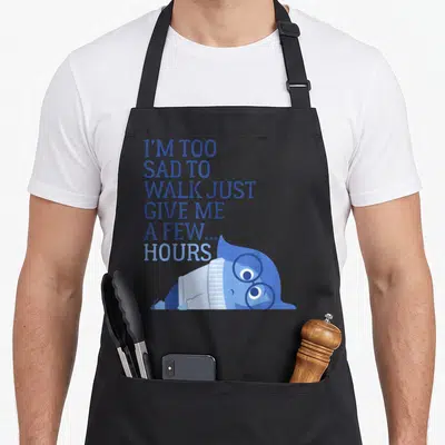 Sad novelty apron - Stacked blue text reading I'm too sad to walk above a lying blue cartoon character with glasses — shown on a black cotton canvas apron against a white background