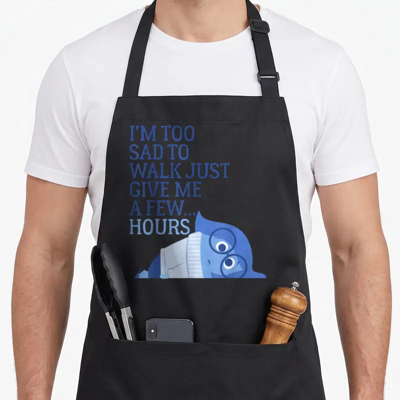 Sad novelty apron - Stacked blue text reading I'm too sad to walk above a lying blue cartoon character with glasses — shown on a black cotton canvas apron against a white background