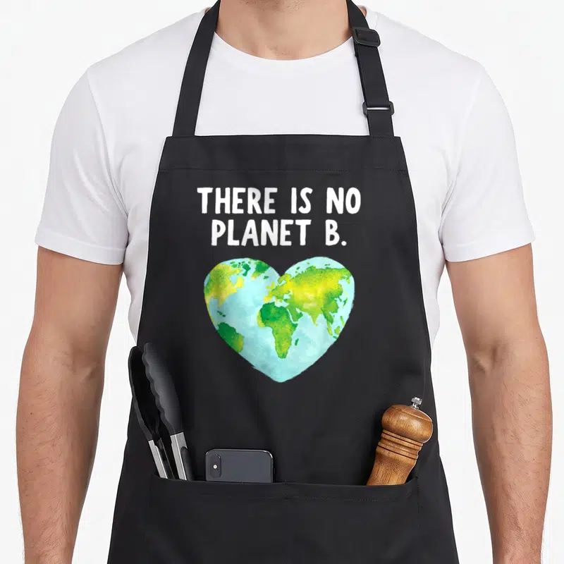 Earth planets apron - White text There Is No Planet B above a watercolor heart shaped earth in blue green and yellow — shown on a black cotton canvas apron against a white background