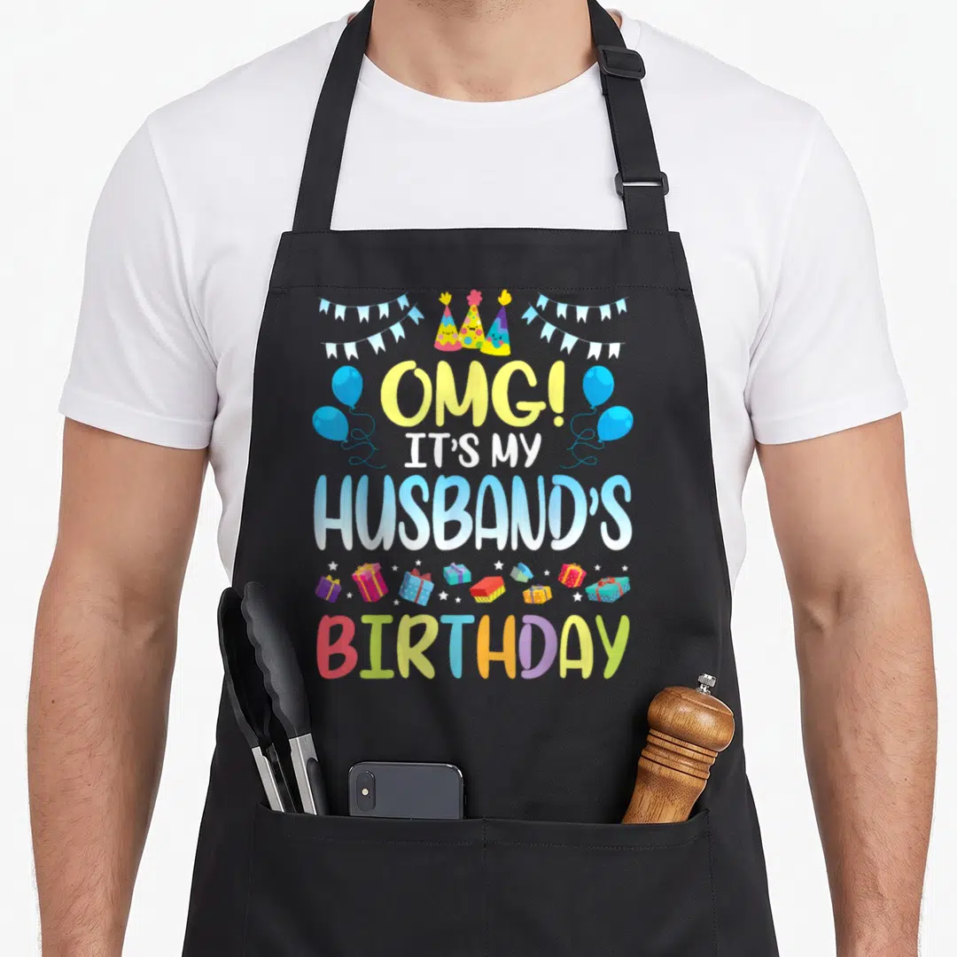 Omg husband apron - Stacked OMG husband birthday text with cartoon party hats, blue bunting, balloons, and colorful — shown on a black cotton canvas apron against a white background