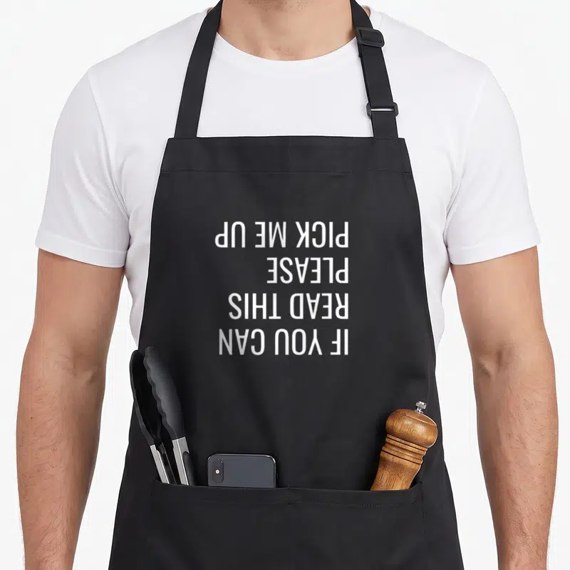 Balance fall apron - White upside-down text reading IF YOU CAN READ THIS PLEASE PICK ME UP — shown on a black cotton canvas apron against a white background